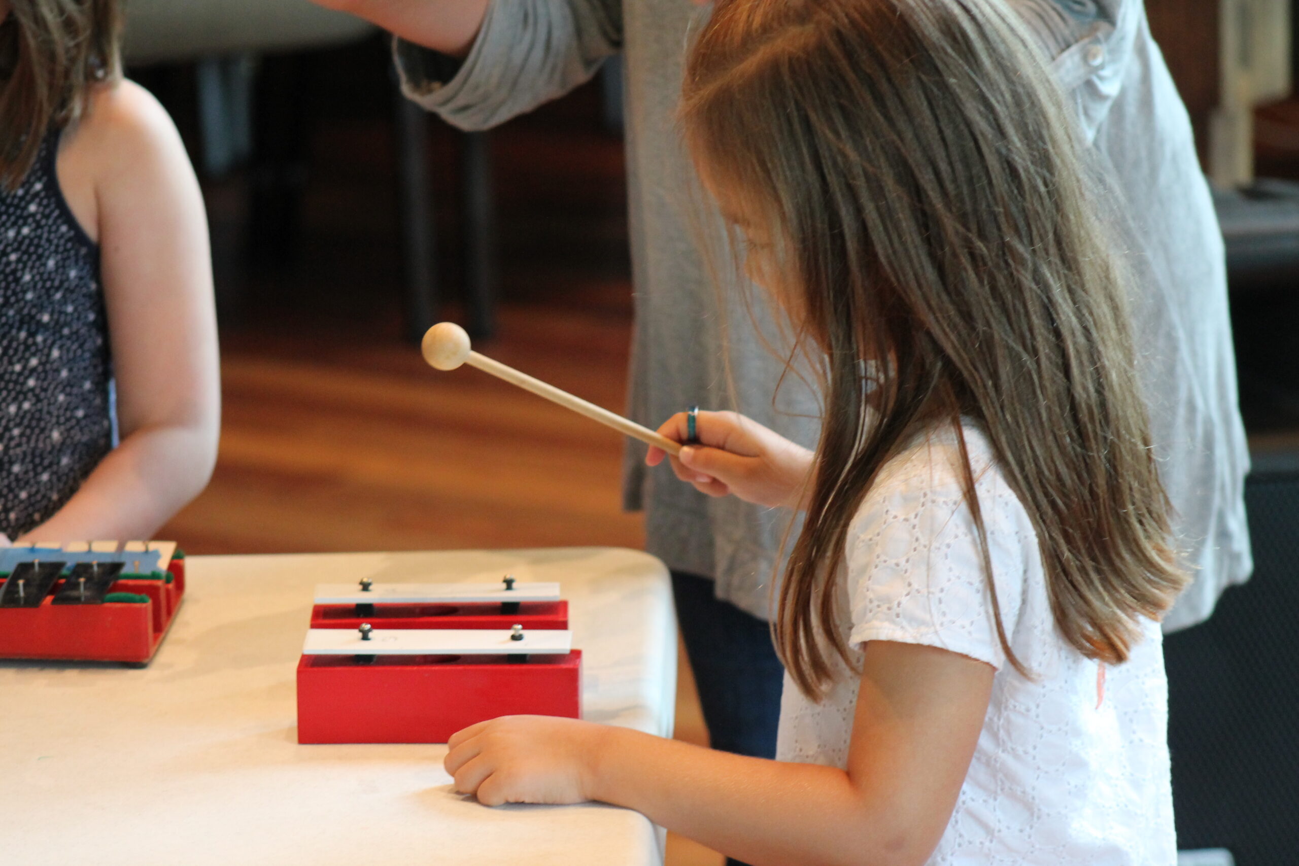 A girl playing a red xylophone with a mallet indoors.