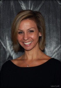 Smiling woman with short hair, dark background.